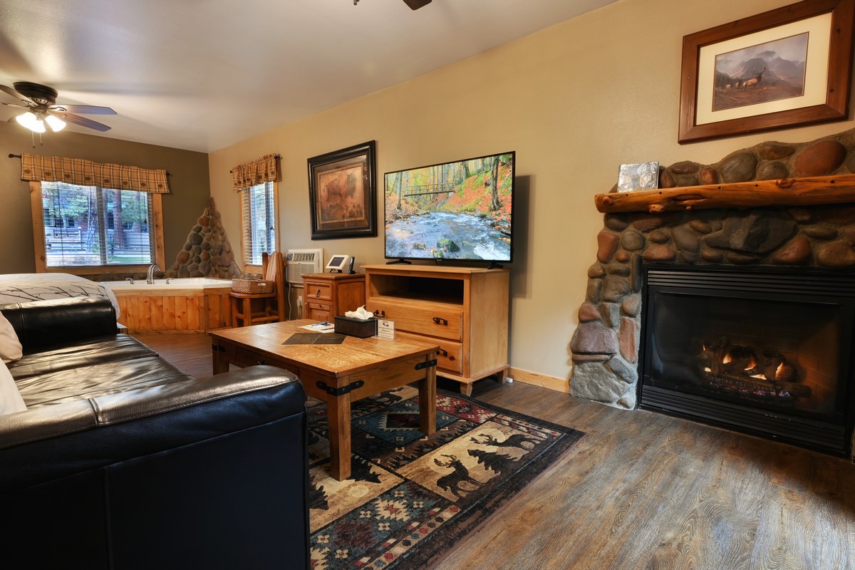 Cozy living room of the Pine Cone Cabin, featuring a gas fireplace, comfortable seating, and large windows with a river view.