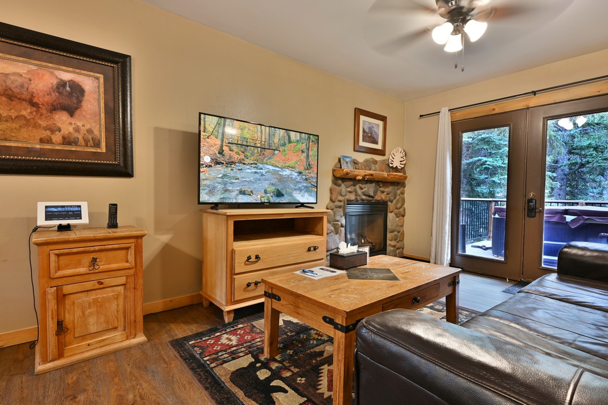 Living area of the Pine Cone Cabin in Estes Park, showing the flat-screen TV, stone fireplace, and private deck with hot tub access.